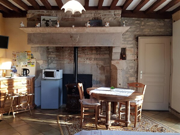 Une cuisine rustique avec une cheminée en pierre, des meubles en bois et un sol carrelé.