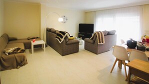 A living room with a sofa, a coffee table, a TV, and a dining area with chairs and a table. - Spacieux Appart à 200m de la Plage de Roses - Terrasse BBQ, Parking Gratuit, 8 pers (Roses)