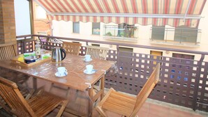 A balcony with a wooden table set for two, a kettle, and a bottle of liquor. - Spacieux Appart à 200m de la Plage de Roses - Terrasse BBQ, Parking Gratuit, 8 pers (Roses)