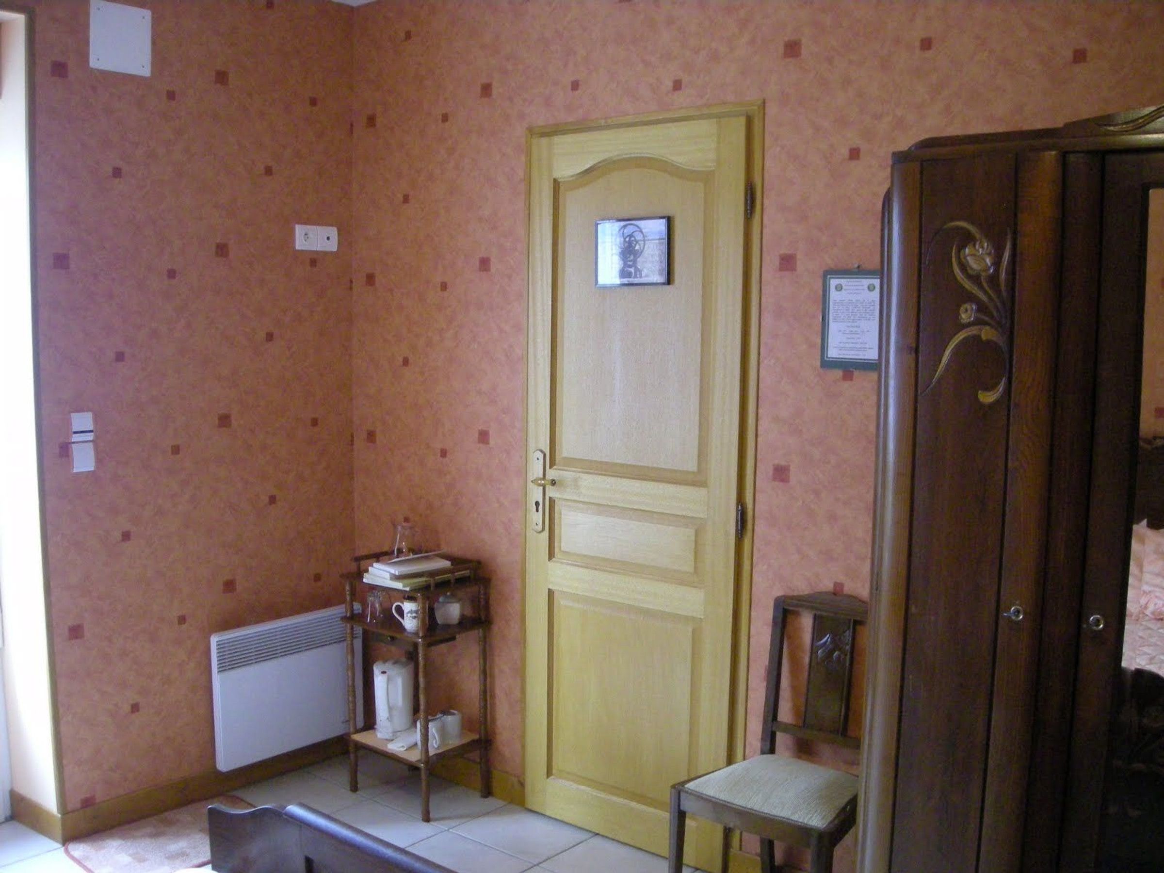 A room with a wooden door, a small table with books and a kettle, a radiator, and a cabinet.