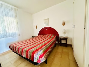 Un lit simple avec une tête de lit rouge, une table de chevet avec une lampe et un luminaire fixé au mur.