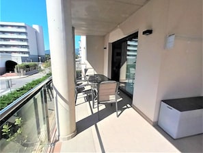 A balcony with a table and chairs, a trash bin, and a glass door leading to an interior space.