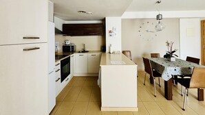 Een moderne keuken met witte kastjes, een eethoek met tafel en stoelen, en een klok aan de muur.