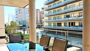 Een balkon met een glazen tafel en stoelen, met uitzicht op een meerlaags gebouw met balkons.