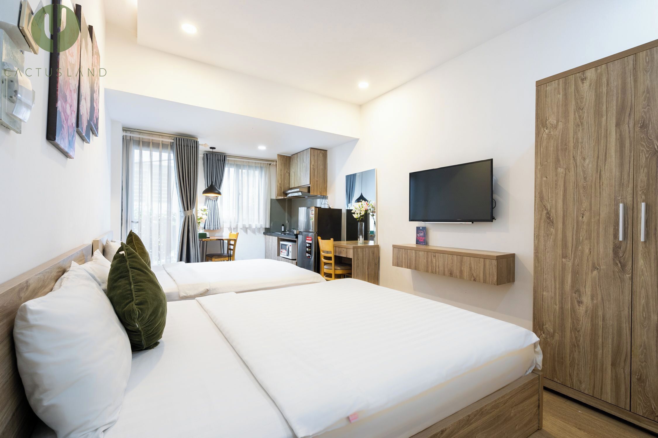 A hotel room with two beds, a TV, a wooden wardrobe, and a kitchenette.