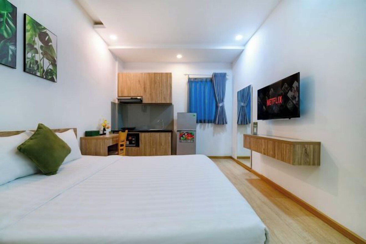 A compact hotel room with a bed, a small kitchenette, a TV, and a wall-mounted shelf.