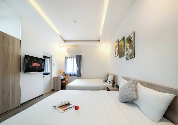 A hotel room with a bed, a desk, a TV displaying 'NETFLIX', and a window with curtains.