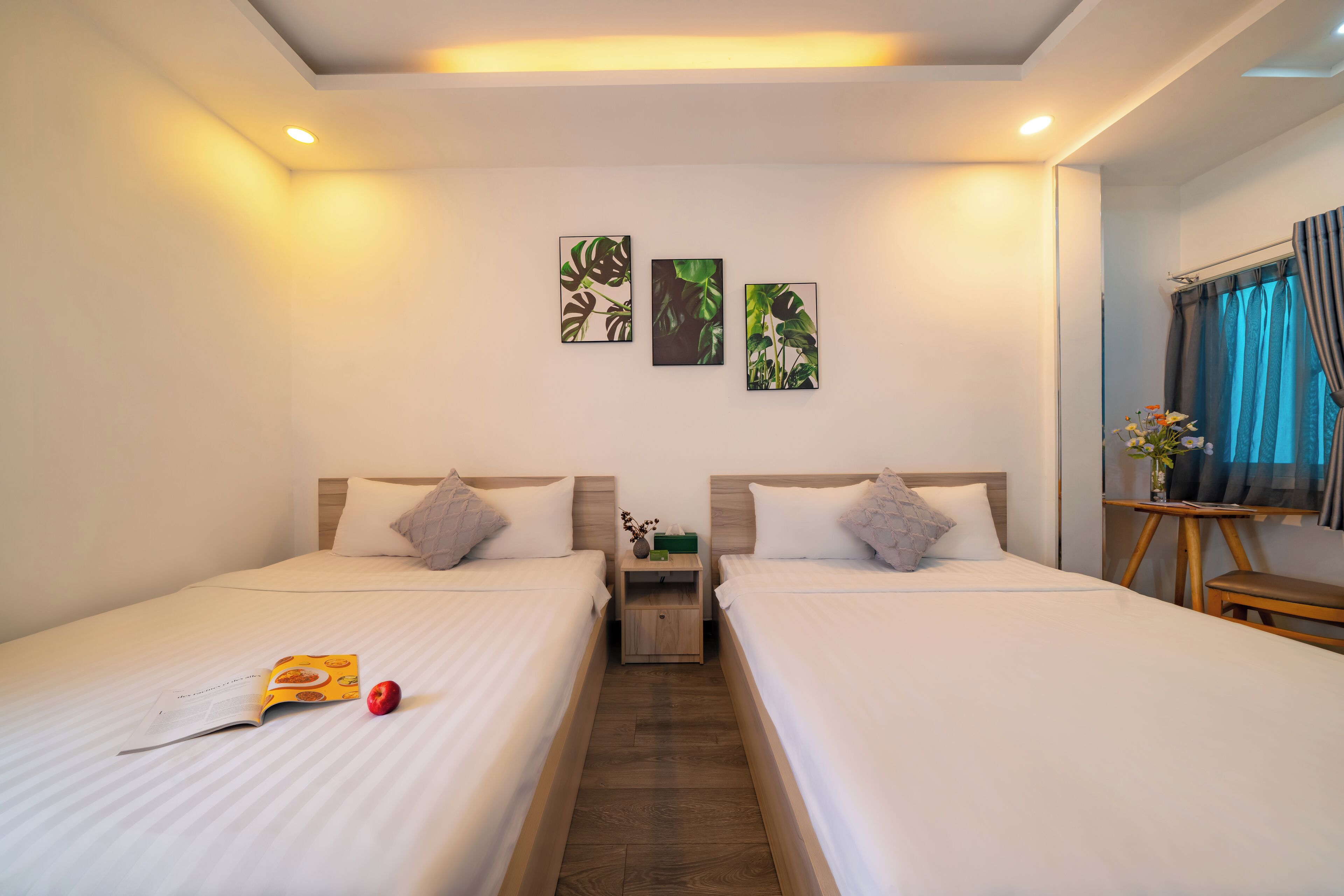 A hotel room with two beds, a nightstand, a small table, and wall art.