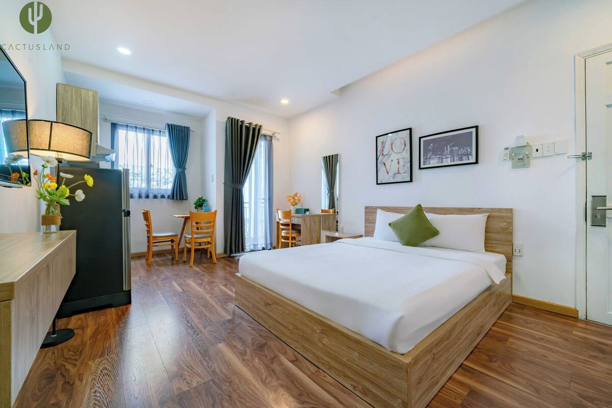 Une chambre d’hôtel avec un lit en bois, un bureau, une chaise et une petite table avec une lampe.