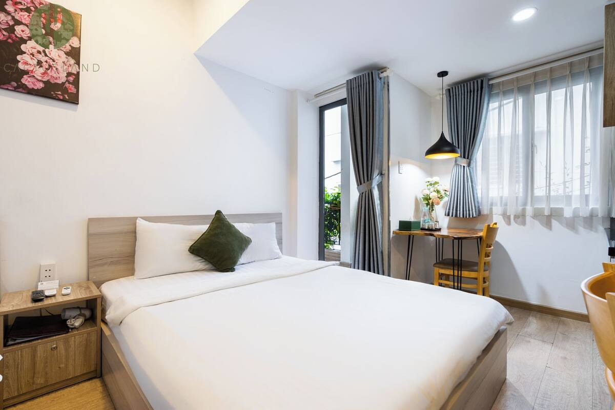 Une chambre d’hôtel avec un grand lit, une table de chevet en bois, un bureau avec une chaise et une fenêtre avec des rideaux.