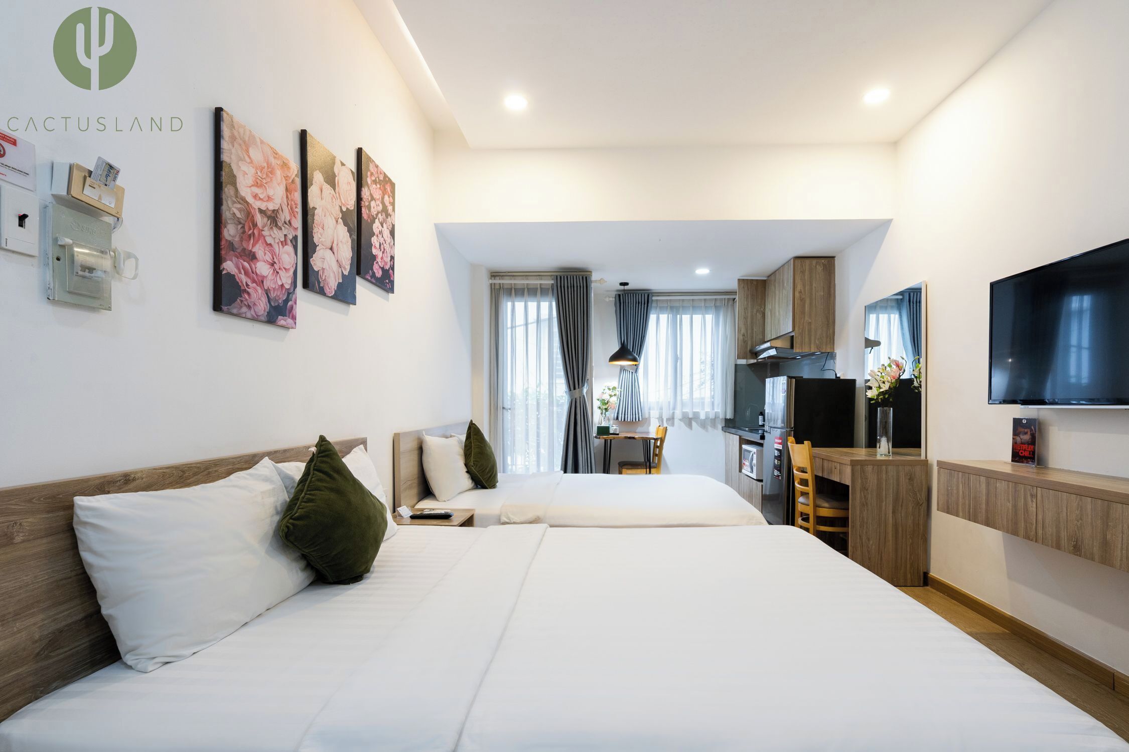 A hotel room with two beds, a kitchenette, a TV, and artwork on the wall.