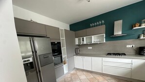 A modern kitchen with stainless steel appliances, white cabinetry, and a teal accent wall.