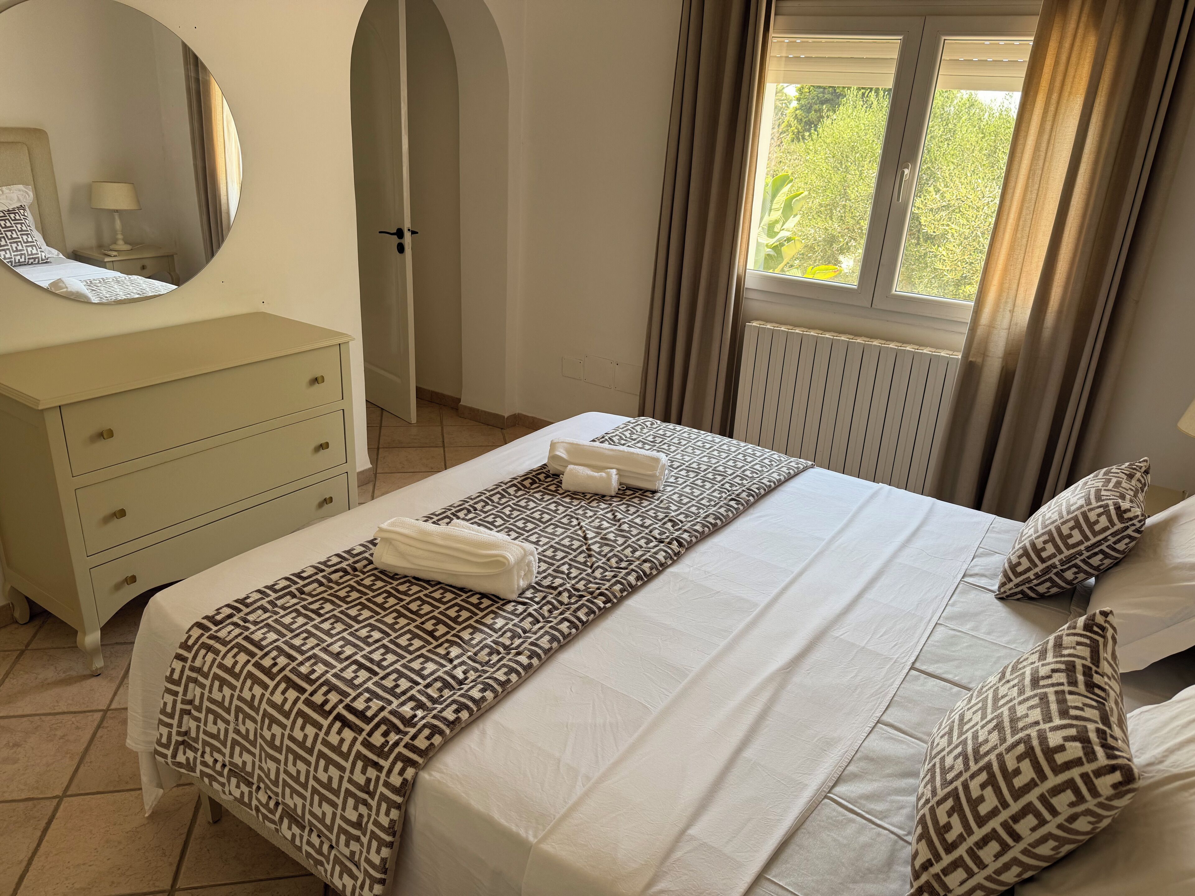 Un lit bien fait, avec une literie à motifs, une table de chevet avec une lampe, une commode et une fenêtre avec des rideaux.