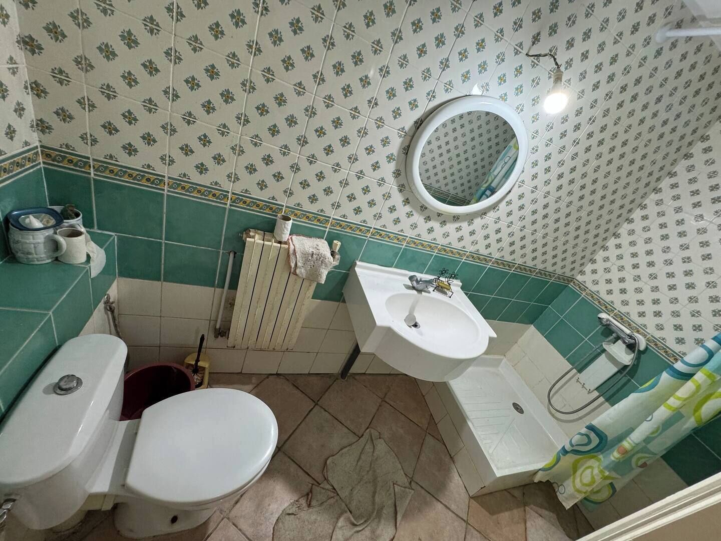 A bathroom with a toilet, sink, and shower area. There is a towel hanging on the radiator, and a mirror on the wall.