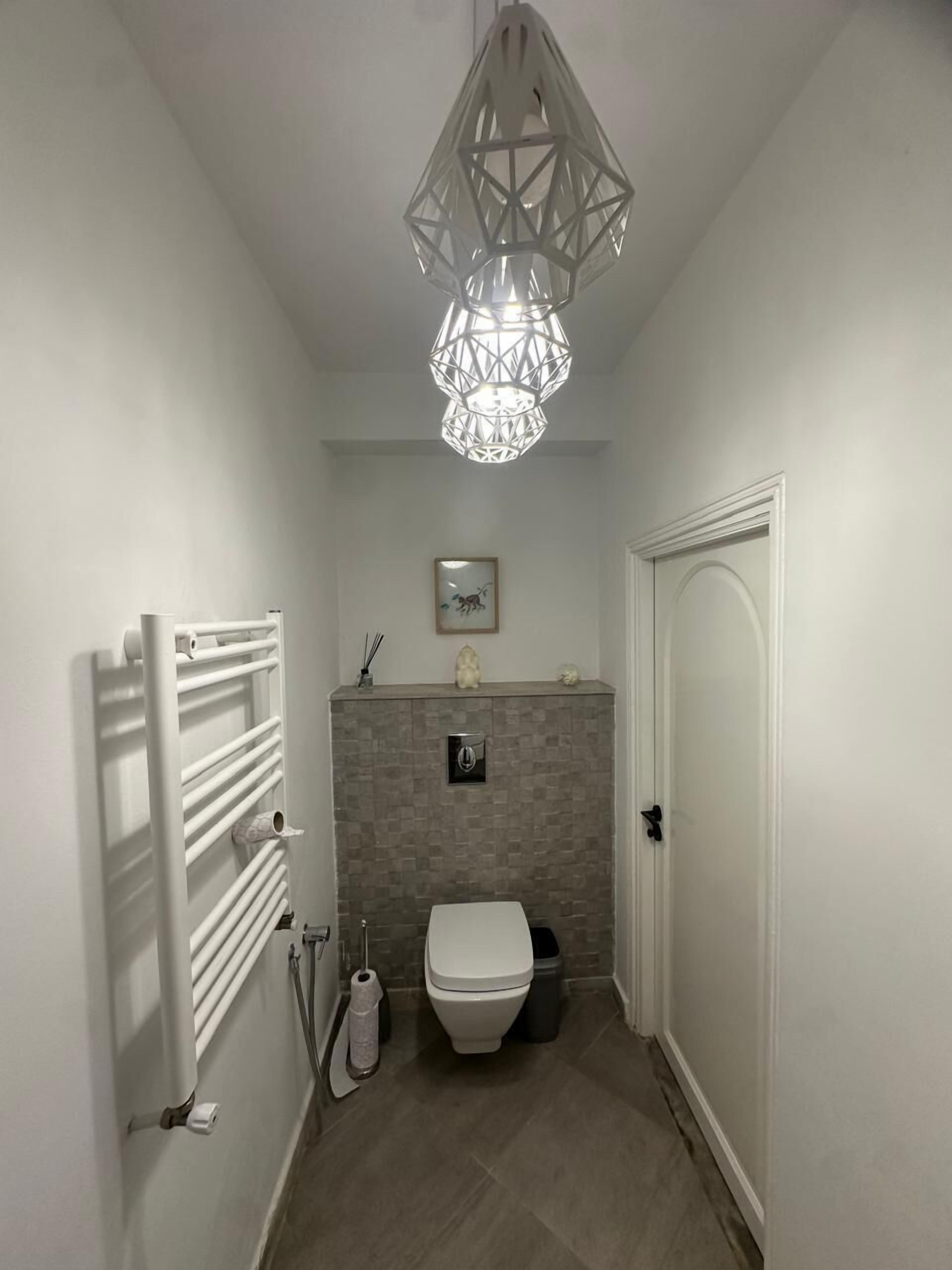 Un baño moderno con inodoro blanco, toallero, ducha y una lámpara decorativa.