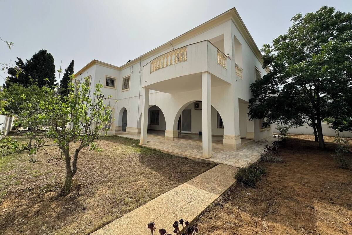 Un edificio blanco con un patio cubierto, paseos con arcos y un letrero que dice "BIBLIOTECA".