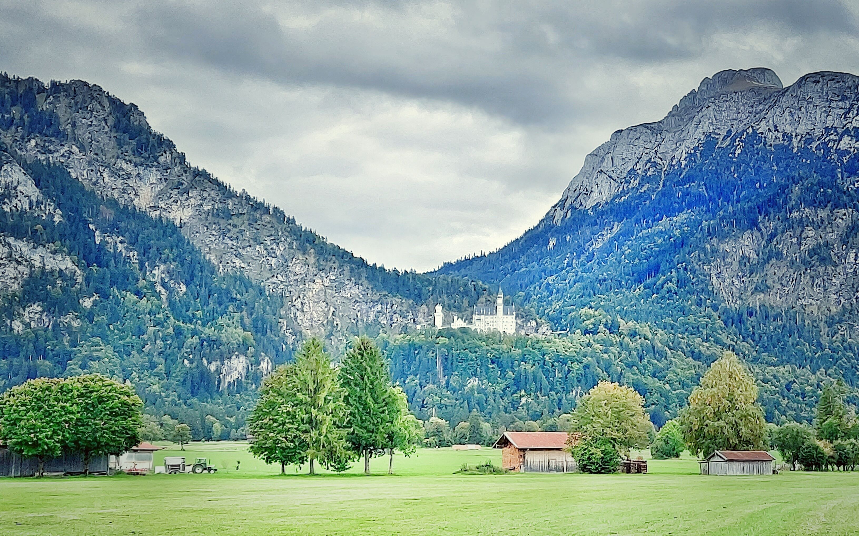 Een kasteel, omringd door bergen en groene velden.