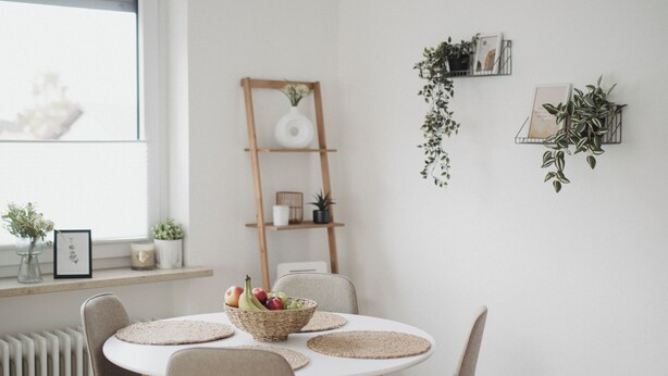 Un coin repas avec une table ronde, quatre chaises, un panier de fruits, une étagère en forme d’échelle et des plantes en pot.
