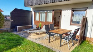 Une terrasse extérieure avec une table et des chaises en bois, un fauteuil de relaxation et un petit coin jardin.
