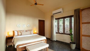 Ein Schlafzimmer mit Bett, Nachttischen, einer Bank, einem Deckenventilator, einer Klimaanlage, einem Fenster mit Vorhängen und einer Topfpflanze.