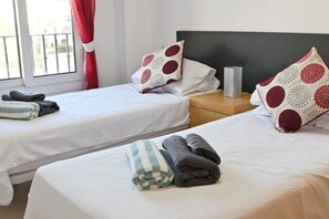 Two twin beds with white bedding and red and white patterned pillows, a bedside table with a lamp, and a window with curtains. - A beautiful pool view apartment - AO1822LT (La Torre Golf Resort)
