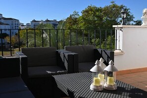 An outdoor seating area with a sofa and tables, surrounded by a black metal fence, and a statue on a pedestal. - A beautiful pool view apartment - AO1822LT (La Torre Golf Resort)