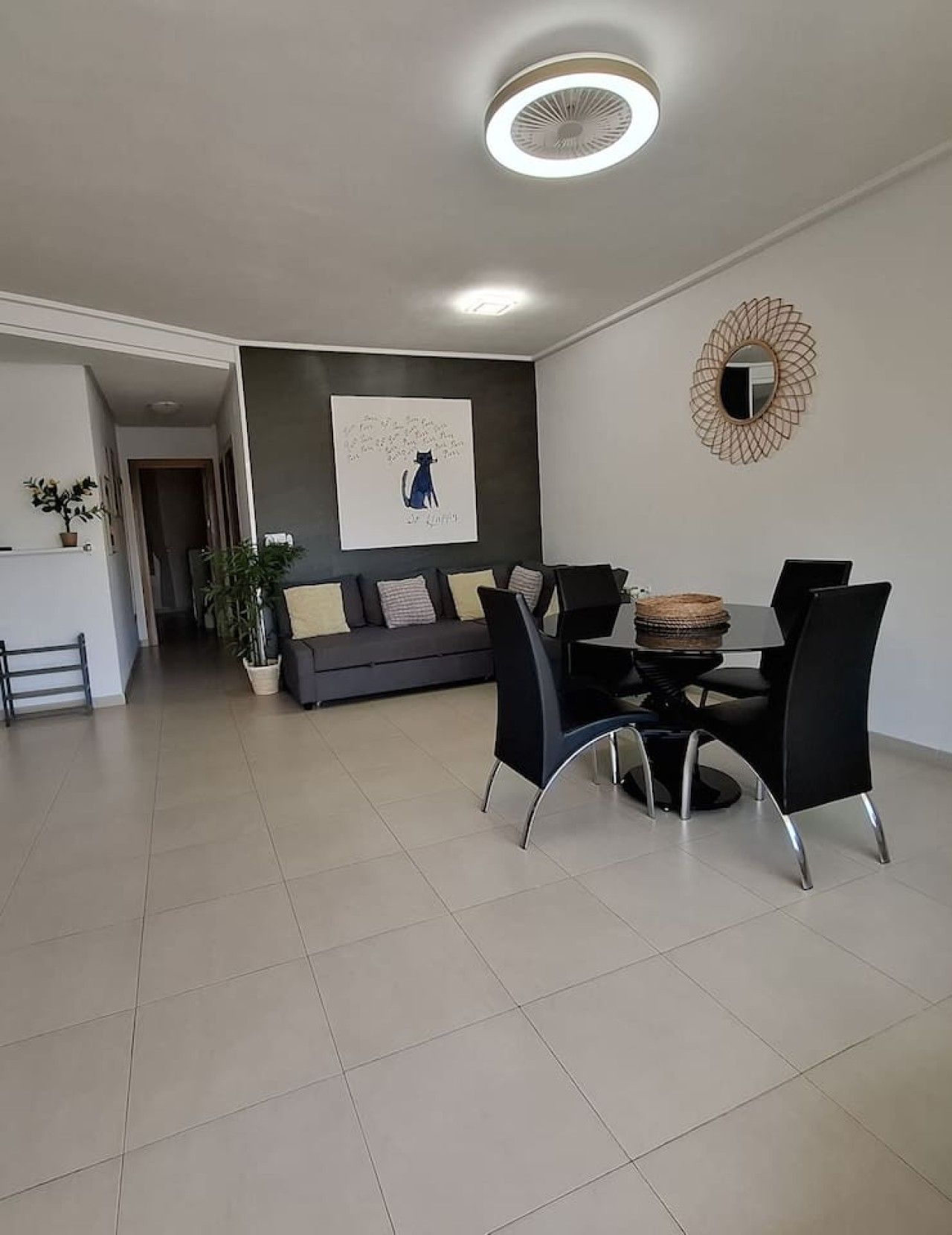 A modern living room with a dining area, a grey sofa, a round table, and a ceiling fan.