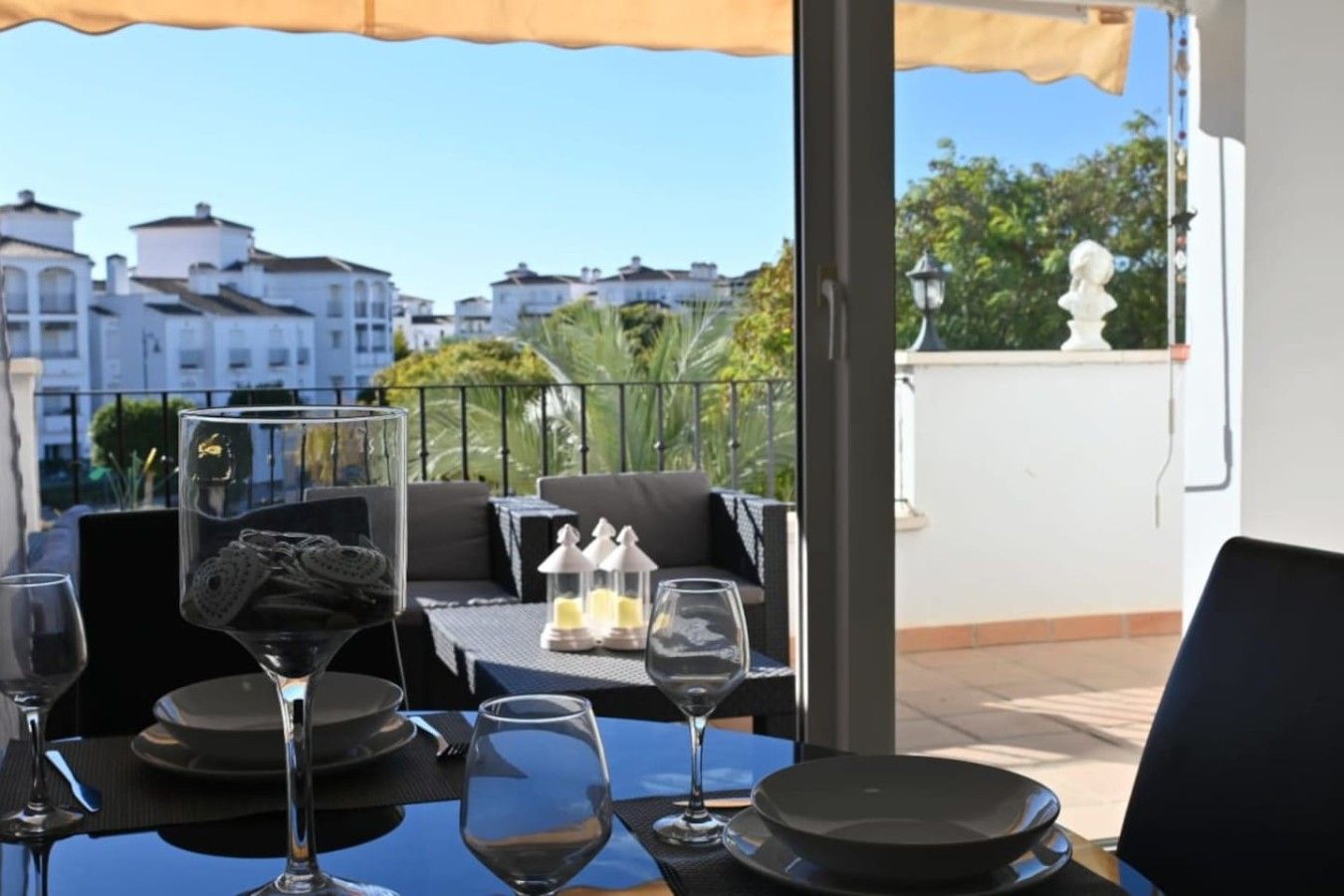 An outdoor dining area with a table set for two, a clear view of the cityscape, and a balcony railing.