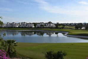 A golf course with a pond, green grass, and white buildings in the background. - Murcia Vacations`s Apartments 1, Apartamento fa... (La Torre Golf Resort)