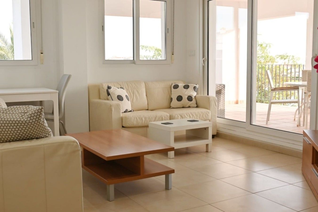 A modern living room with a sofa, two coffee tables, and a view of the outside balcony.