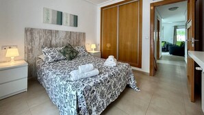 A bedroom with a bed, nightstands, a wardrobe, and a hallway leading to another room. - Groundfloor apartment next to the pool - ER702LT (La Torre Golf Resort)