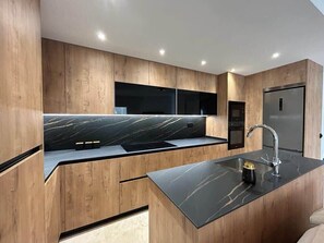 A modern kitchen with wooden cabinetry, a black marble countertop, and a stainless steel sink.