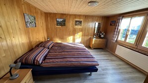 A wooden-paneled bedroom with a bed, dresser, and artwork on the walls. - Ferienwohnung Gehrihorn by Interhome (Frutigen)
