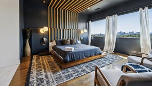 A modern bedroom with a large bed, a city view, and a unique ceiling design.