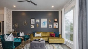 A modern living room with a sofa, chairs, and a coffee table. There are wall decorations and a large window.