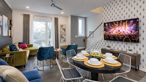 A modern living room with a dining area, a large flat-screen TV, and a staircase leading to another level.