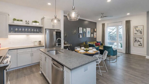 A modern kitchen with a central island, stainless steel appliances, pendant lighting, and a dining area with a view of the outdoors.