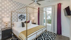 A bedroom with a four-poster bed, a ceiling fan, a TV on the wall, and patterned wallpaper.