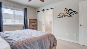 Un dormitorio con cama, ventilador de techo, puerta corredera y un adhesivo mural con montañas.