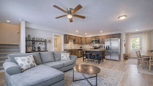 Una cocina moderna con una isla central, un comedor con mesa y sillas, y una sala de estar con sofá y una mesa de centro.