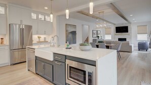 A modern kitchen with stainless steel appliances, a large island, pendant lighting, and a dining area with a TV. - Spacious Montana home near Big Sky and BZN airport (Belgrade)
