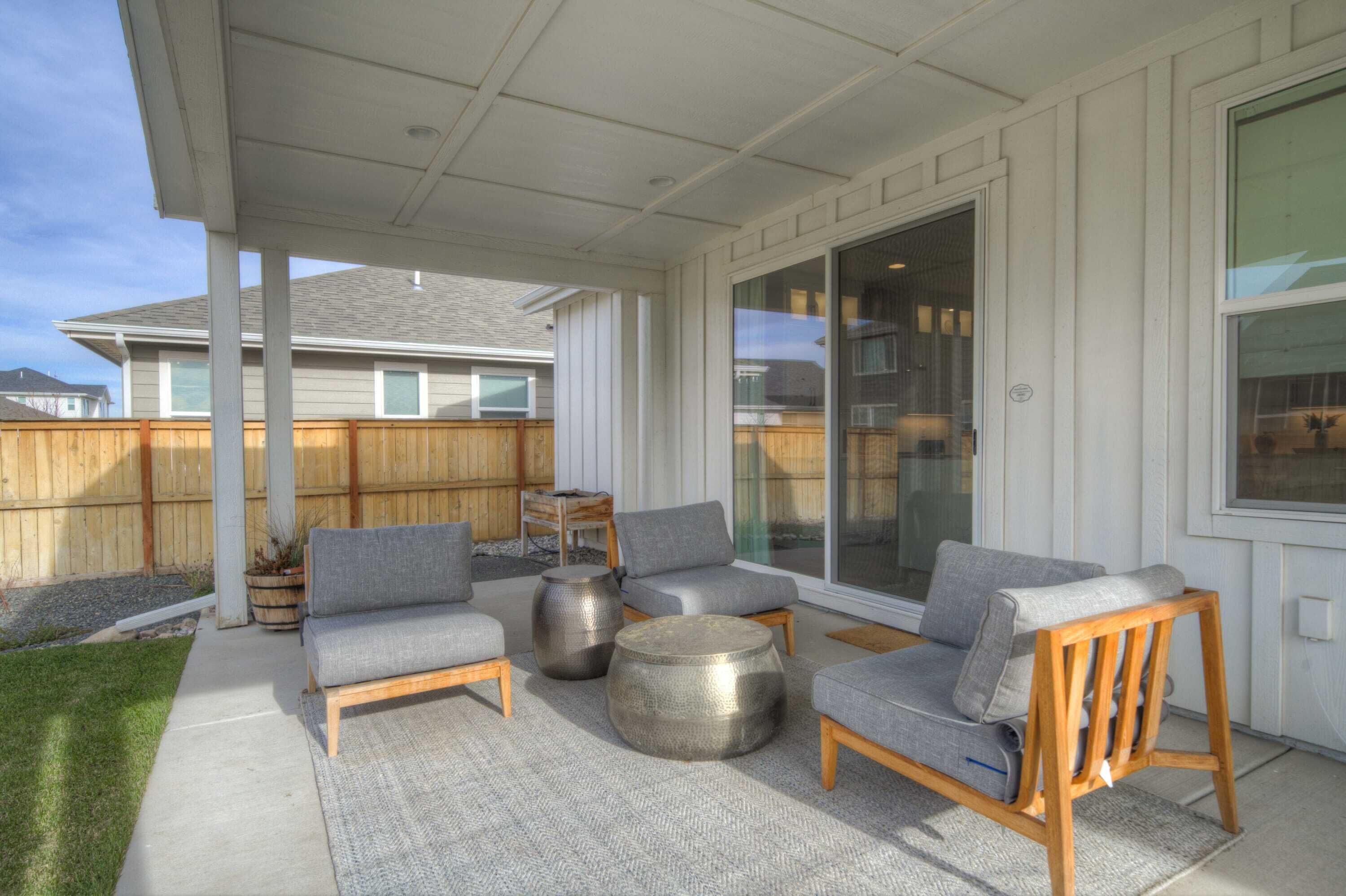 A covered patio with grey sofas, round metal tables, and a wooden chair.
