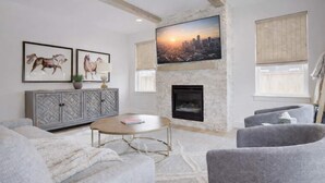 A modern living room with a fireplace, a large TV mounted on the wall, and a cityscape view. - Spacious Montana home near Big Sky and BZN airport (Belgrade)