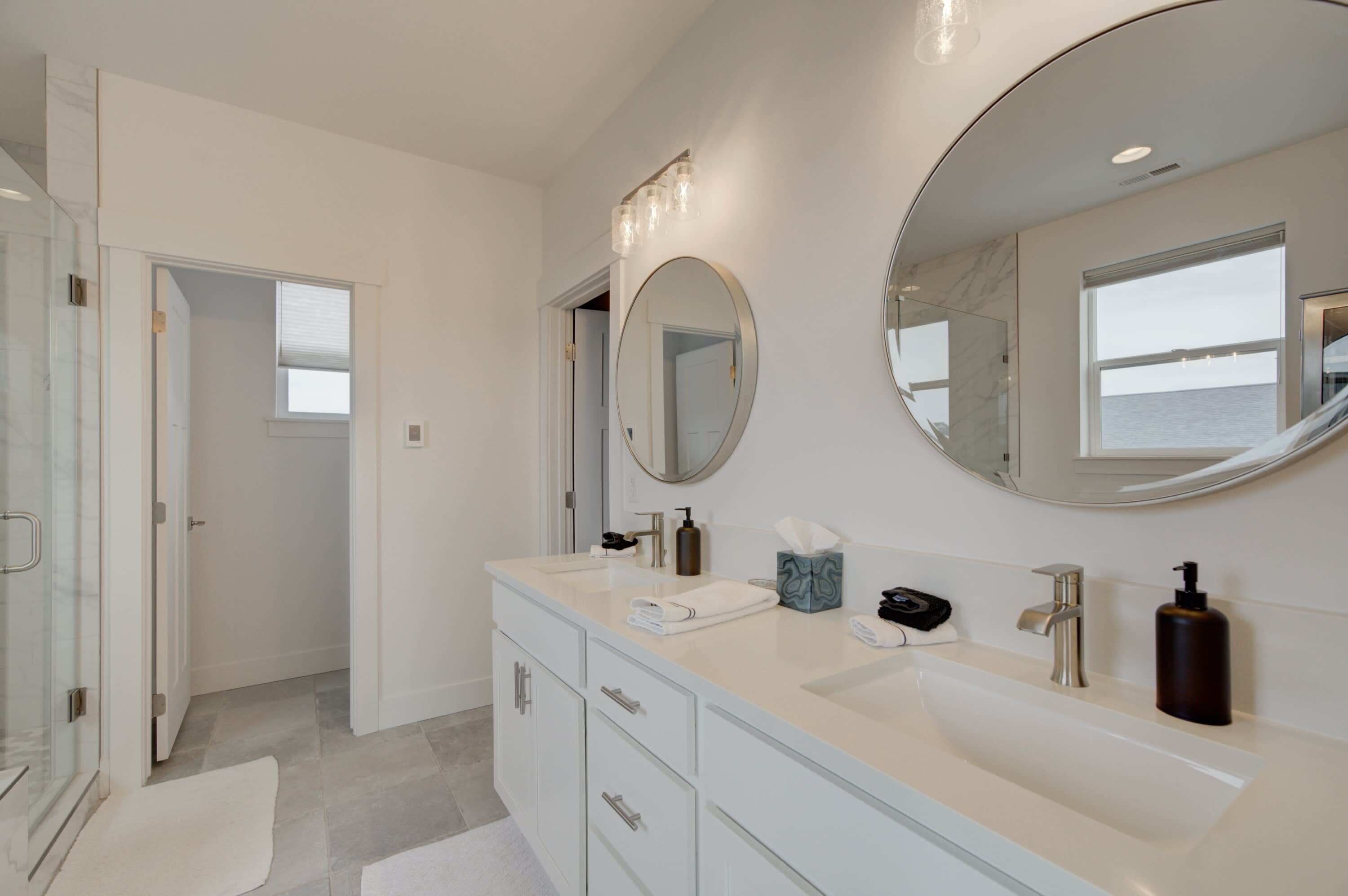 A modern bathroom with a large sink, two mirrors, and a walk-in shower.