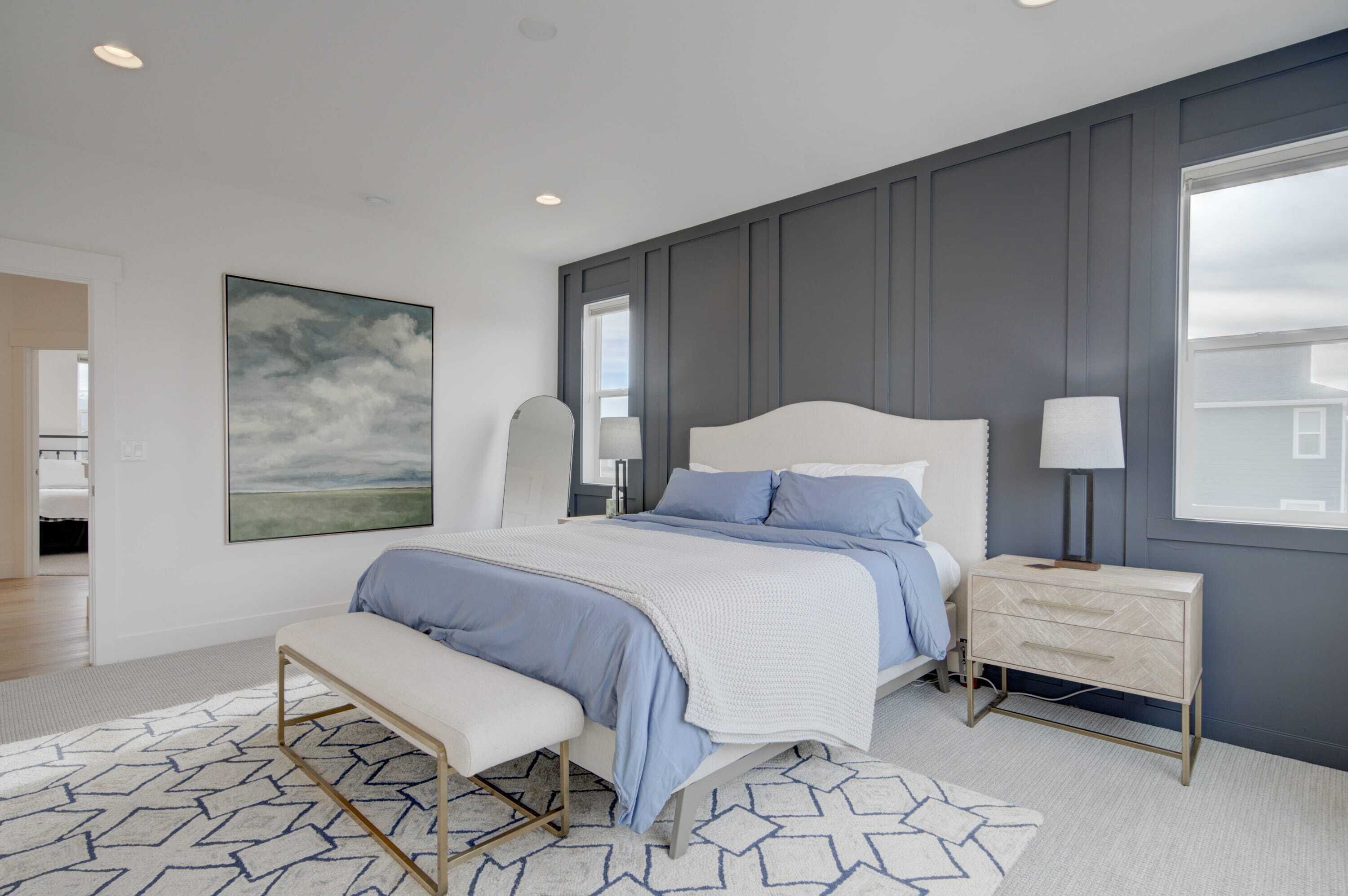 A bedroom with a bed, bedside table, bench, and a large window.