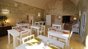 Un espace repas avec des tables et des chaises blanches, des murs en pierre et une cheminée.