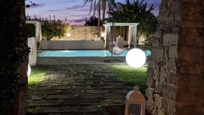 Un chemin de pierre mène à un espace piscine agrémenté d’un fauteuil suspendu et d’une lanterne.