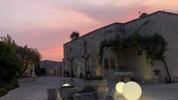 Une cour extérieure avec un bâtiment en pierre, de grandes lampes sphériques et un ciel au coucher du soleil.
