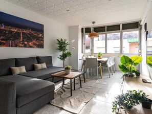 Een moderne woonkamer met een grijze bank, een eettafel met stoelen en een groot raam met uitzicht op de stad.