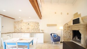 Um quarto acolhedor com parede de pedra, lareira, mesa de jantar com cadeiras e uma poltrona azul.